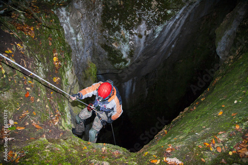 A speleologist man exploring a huge hidden cave hanging on a rope for safety and preparing to go down into the cave