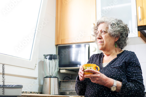 Elderly woman drinks cup of coffee in the kitchen of her home.