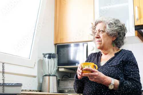Canvastavla Elderly woman drinks cup of coffee in the kitchen of her home.