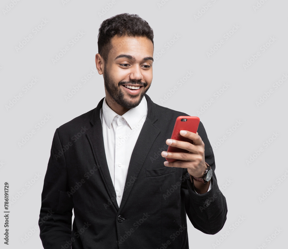 Portrait of handsome cheerful smiling young man using smartphone isolated on gray background. Laughing joyful men with mobile phone studio shot