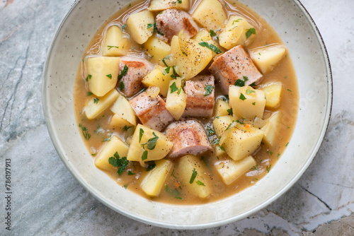Plate of Dublin coddle or Irish sausage and potato stew, horizontal shot on a grey granite surface, elevated view, middle close-up