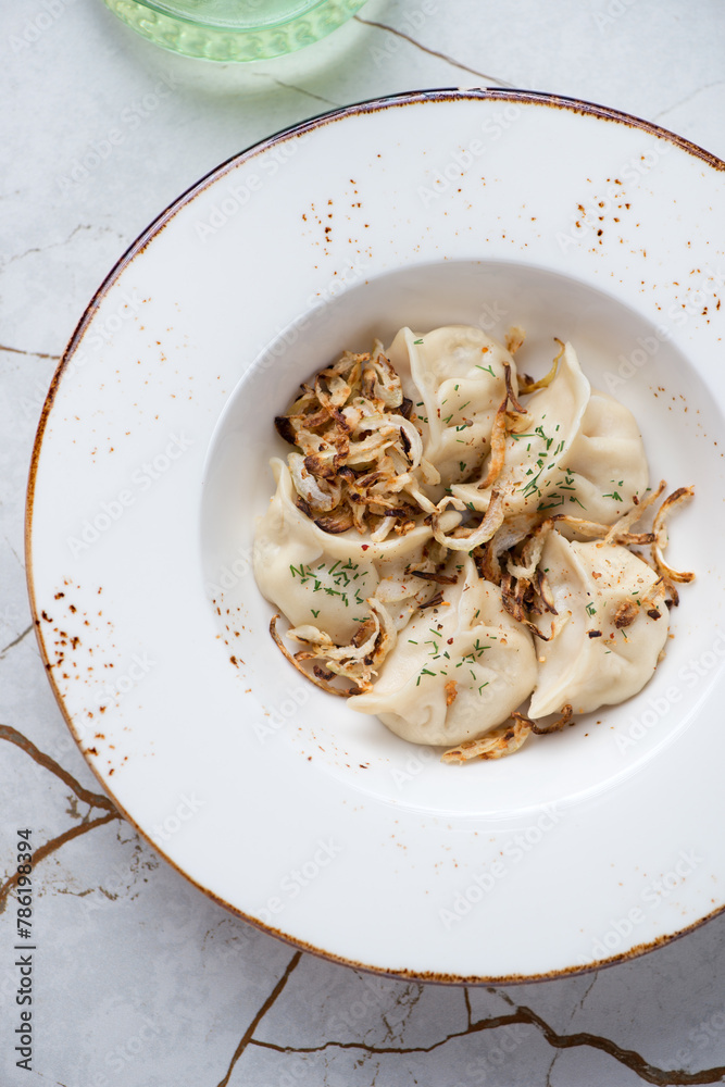 Plate of vareniki dumplings with caramelized onion, vertical shot on a white granite background, flat lay