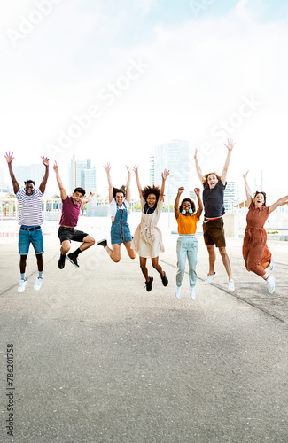Vertical photo of happy multiracial people jumping together outdoors. Friendship concept with group of young friends from diverse cultures and races having fun with city background. Copy space.