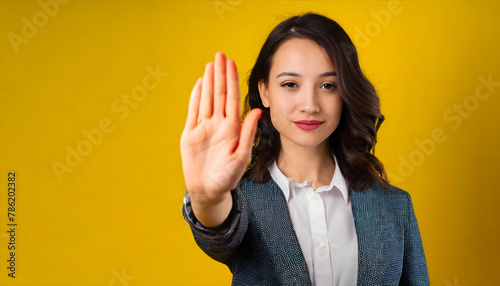 Portrait of an assertive woman with a stop halt hand gesture on yellow background.