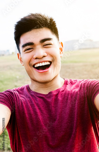 Vertical self-portrait of happy asian young man laughing at city park. Youth people and happiness concept