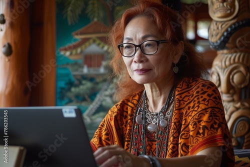 Elderly Asian woman writing note in a book while looking to her laptop computer photo