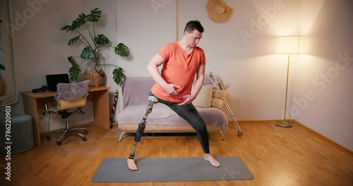 Man amputee with prosthetic leg disability on transfemoral leg prosthesis artificial device making stretching rehabilitation physical exercise at home. People w amputation disabilities everyday life photo