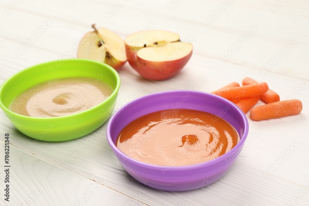 Baby food. Purees of apples and carrots in bowls on white wooden table Baby food. Purees of apples and carrots in bowls on white wooden table