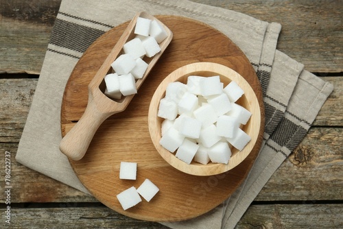 White sugar cubes in bowl and scoop on wooden table, top view