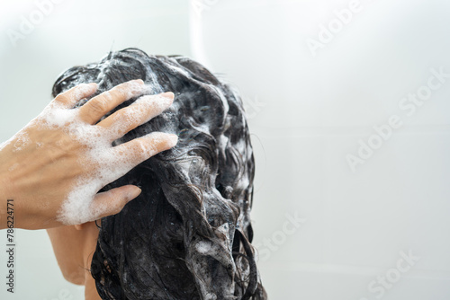Young woman washing her hair with shampoo foaming. Female rubbing hair and scalp and taking a shower with foam on her head holds fingers in hair in bathroom. Hands to massage head while washing hair.