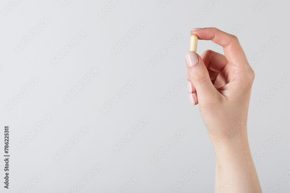 Woman holding vitamin capsule on light grey background, closeup with space for text. Health supplement - obrazy, fototapety, plakaty 
