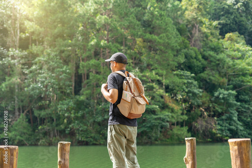 Young happy man standing and looking at distance enjoying the fresh air in the forest and river. Male hiker with backpack and map with open arms enjoying and relax the nature.