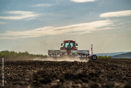 rear view of a working tractor with seeder with dust raising up in ploughed field