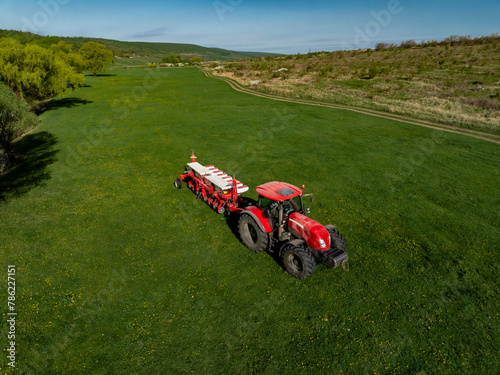 aerial view of red tractor with seeder on green grass during sunny day