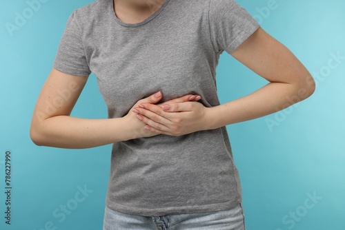 Woman suffering from stomach pain on light blue background, closeup