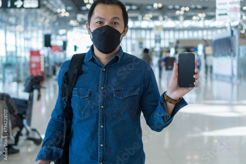 Asian man passenger wearing protective face mask showing e-ticket to flight. Touris man showing boarding pass on mobile phone. Young male showing smartphone at airport. photo