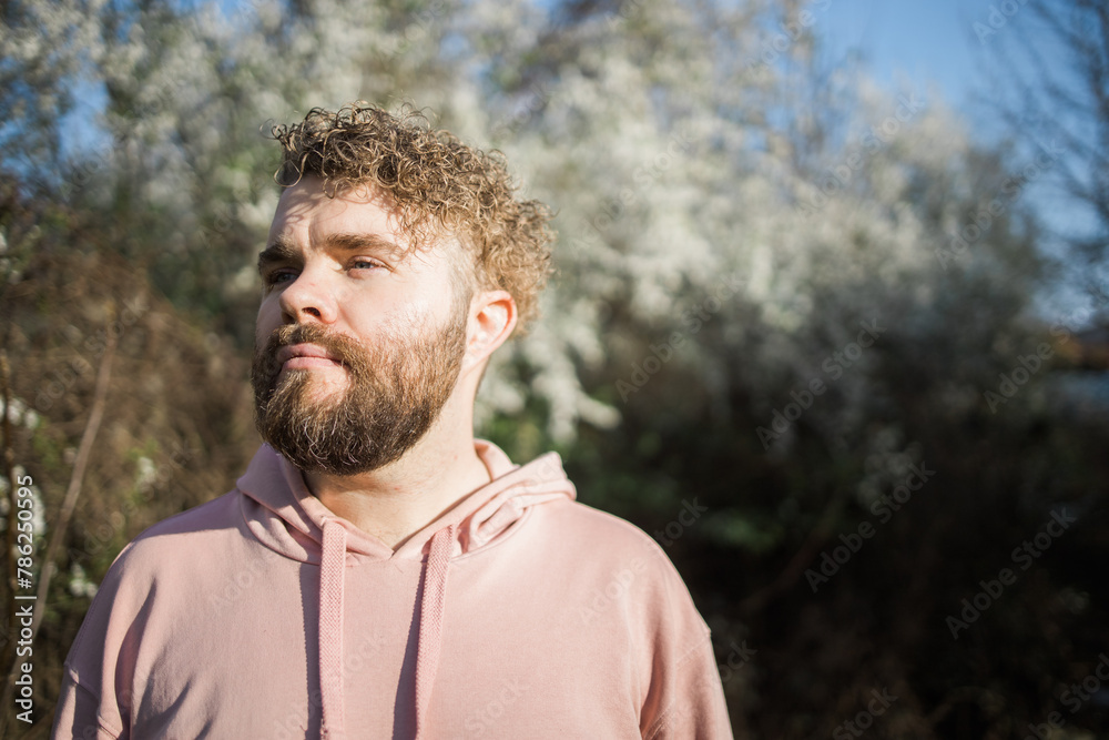Male bearded man standing under branches with flowers of blooming almond or cherry tree in spring garden. Spring blossom. Copy space Male bearded man standing under branches with flowers of blooming almond or cherry tree in spring garden. Spring blossom. Copy space