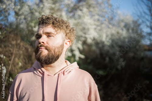 Male bearded man standing under branches with flowers of blooming almond or cherry tree in spring garden. Spring blossom. Copy space