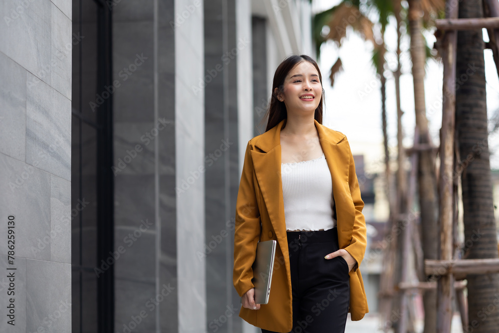 Fototapeta premium businesswoman lifestyle - Portrait Successful business woman in yellow suit walking outdoors with laptop computer on street office building. walking city urban street at business office center.