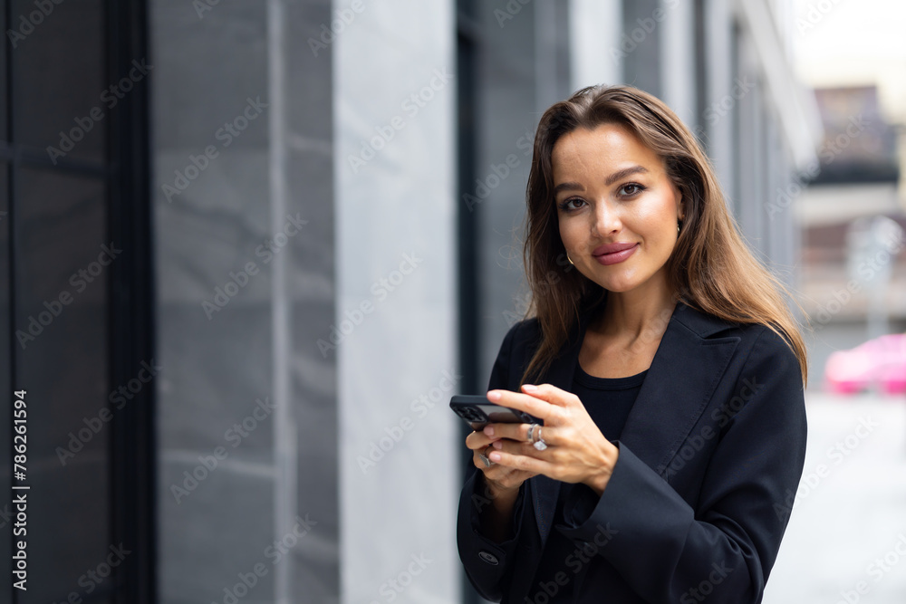 Mobile phone technology lifestyle - Hispanic business woman uses mobile phone device communicating with a colleague. Female walking outside modern office building