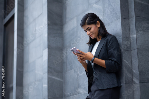 Mobile phone technology lifestyle - Portrait Smiling Young Businesswoman in black suit using smartphone at outside modern office building