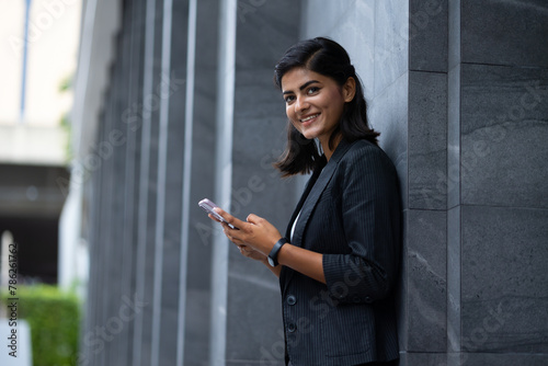 Mobile phone technology lifestyle - Portrait Smiling Young Businesswoman in black suit using smartphone at outside modern office building