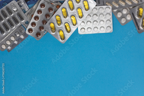 Many colorful blisters pills, capsules blue background, copy space, top view, mockup, flat lay. Pharmacology, treatment, omega, vitamins, disease prevention, antibiotic, macro image, hi-res banner