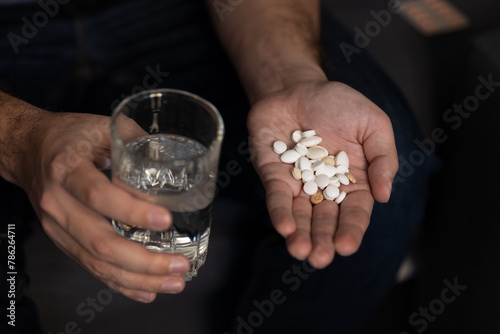Taking many different pills man's hand glass water. Selective focus, taking vitamins, pill overdose, disease treatment, mental, depression, dramatic concept, sleeping pills, suicide. world, day