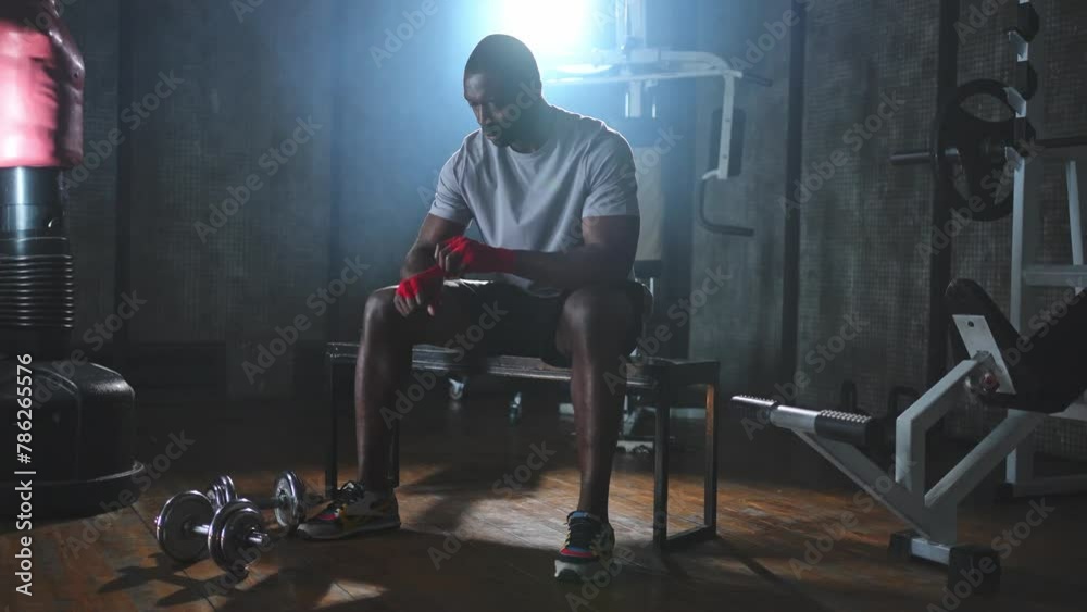 Fitness workout in gym. African American man fighter preparing for fight wrapping hands with red boxing wraps sports protective bandages in gym. Strong man ready for fight boxing sparring training Fitness workout in gym. African American man fighter preparing for fight wrapping hands with red boxing wraps sports protective bandages in gym. Strong man ready for fight boxing sparring training