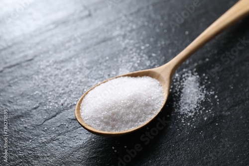 Organic white salt in spoon on black table, closeup
