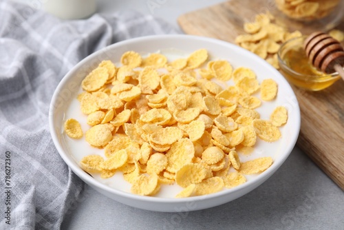 Breakfast cereal. Corn flakes and milk in bowl on light grey table, closeup