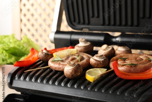 Electric grill with homemade sausages, bell pepper and mushrooms on table, closeup