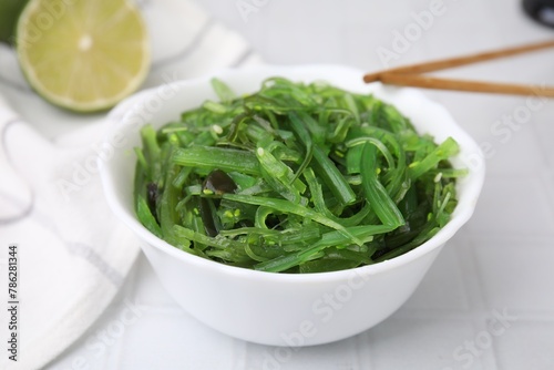 Tasty seaweed salad in bowl served on white tiled table, closeup
