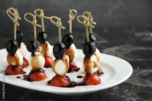 Tasty canapes with black olives, mozzarella and cherry tomatoes on dark textured table, closeup
