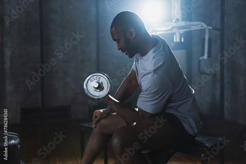 Fitness workout in gym. African American man bodybuilder picking up dumbbells in gym. Workout weight training biceps muscles with dumbbell in fitness club. Man doing sports exercise. Healthy lifestyle