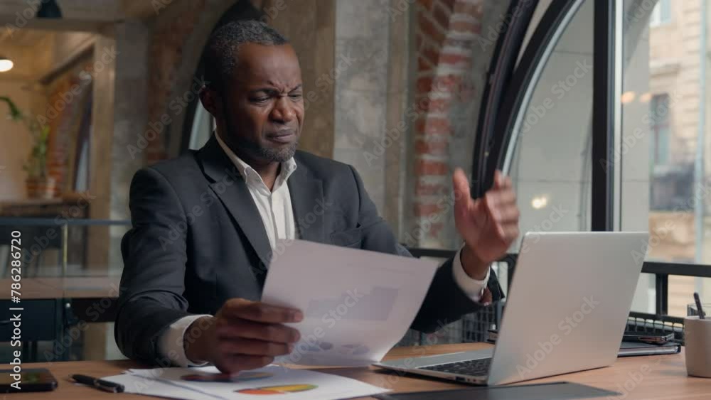Stressed upset failure paperwork stress problem troubled African American entrepreneur with laptop report check data in papers dissatisfied mistake bad result business man office businessman male guy
