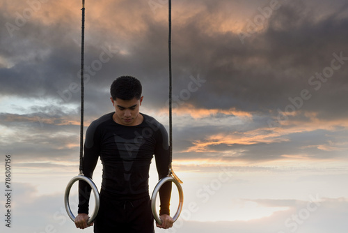 Muscle-up exercise young man doing intense workout at outdoor gym on gymnastic rings photo