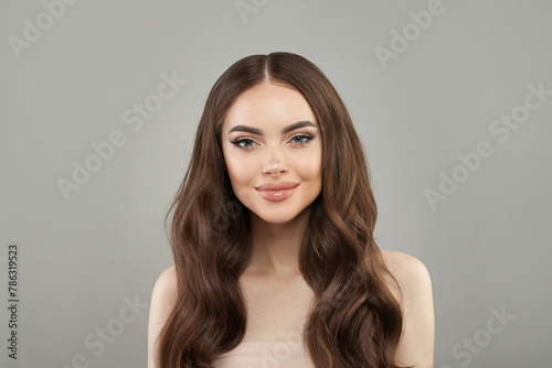 Pretty young happy woman model with natural make-up, clean healthy fresh skin and long hair posing on white background. Curly, haircare, skincare and facial treatment concept