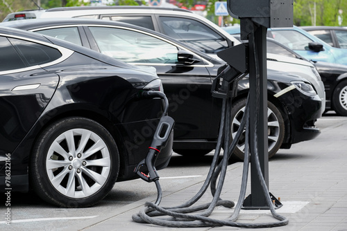 A line of electric cars with alloy wheels is getting charged in a parking lot. Electric cars are charged with ecological renewable energy.