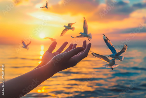 Hands open palm up worship with birds flying over calm water sunset background. Concept of praying for blessing from God. © VisualProduction