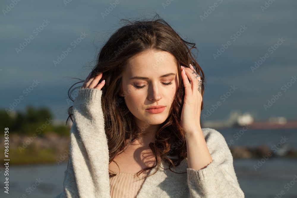 Beautiful young woman model with brown hair and natural make-up walking along the shore of the resort on a spring morning. Happiness, balance, tranquility, emotion and mood concept