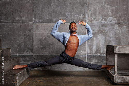 Attractive African American man showcases flexibility and balance, performing leg splits and dancing gracefully indoors. Man stretching