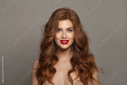 Lovely young happy woman model with natural make-up, clean healthy fresh skin and long hair posing on gray background. Curly, haircare, skincare and facial treatment concept