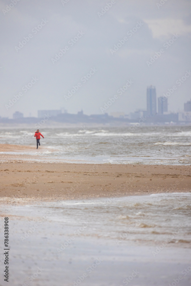 Obraz premium A beautiful walk by the sea. Magnificent sandy beach. Strong waves and various city buildings in the background. Blue and yellow colors of the North Sea.