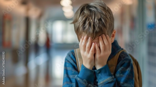 Bullying exclusion at school - Sad lonly teenager boy alone in the school hallway with his hands in front of his face photo