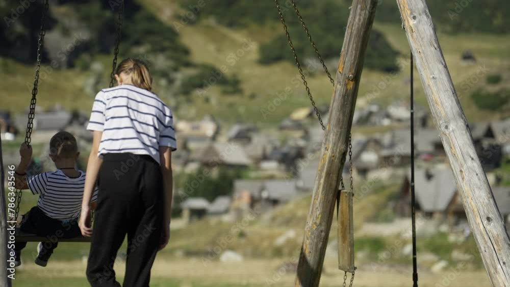 Sister Pushing Brother on a Swing Nearby Mountain Village. Concet of Bonding, Siblings' Help, Childhood Fun