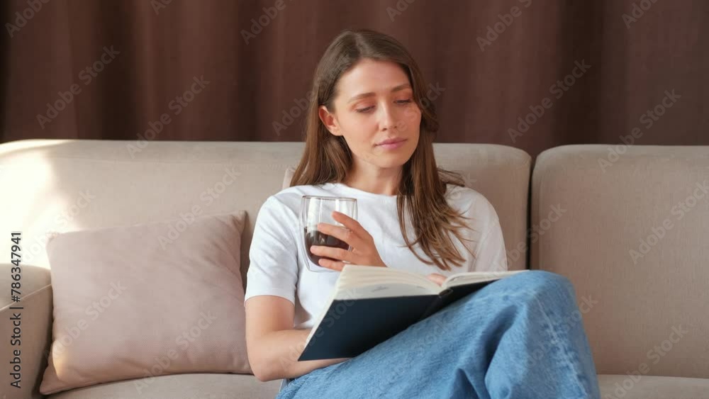 Cheerful caucasian young woman reading a book and drinking cup of coffee and sitting on sofa. Cheerful caucasian young woman reading a book and drinking cup of coffee and sitting on sofa.