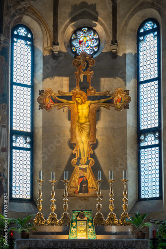 Medieval fresco of crucifix decorating wall behind altar with golden candlesticks inside ancient italian church