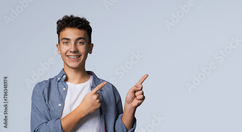 Excited happy black curly haired man in braces, wear denim shirt advertise show peek pointing area for sale slogan text, isolated against grey gray background. Dental care ad advertisement concept.