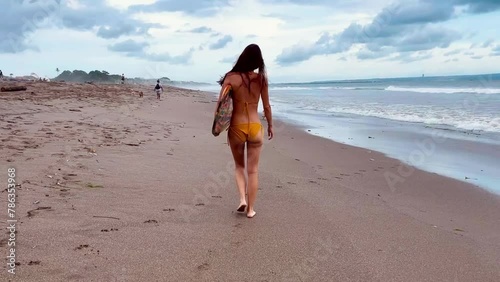 Female surfer. Young woman surfer in bikini goes along tropical beach confidently carrying surfing board on the at sunset. Girl in swimsuit enjoying water sport. High quality FullHD footage